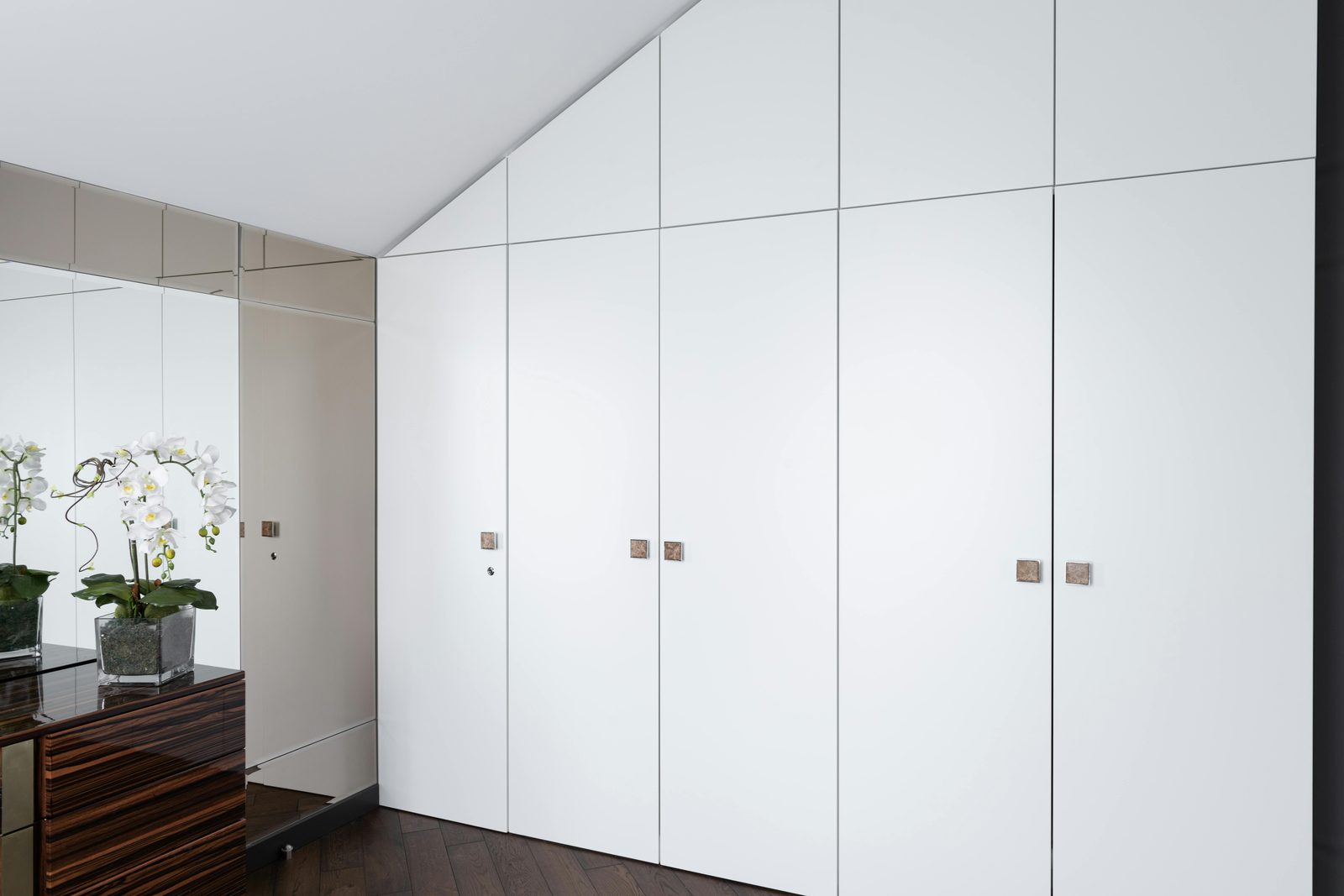 Floor-to-ceiling white wardrobes built into a sloping eaves bedroom