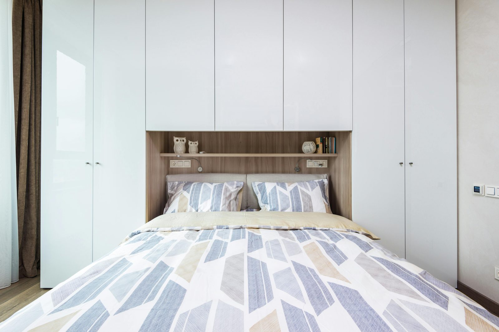 Bridging over-bed storage with display shelving and full-height wardrobes either side