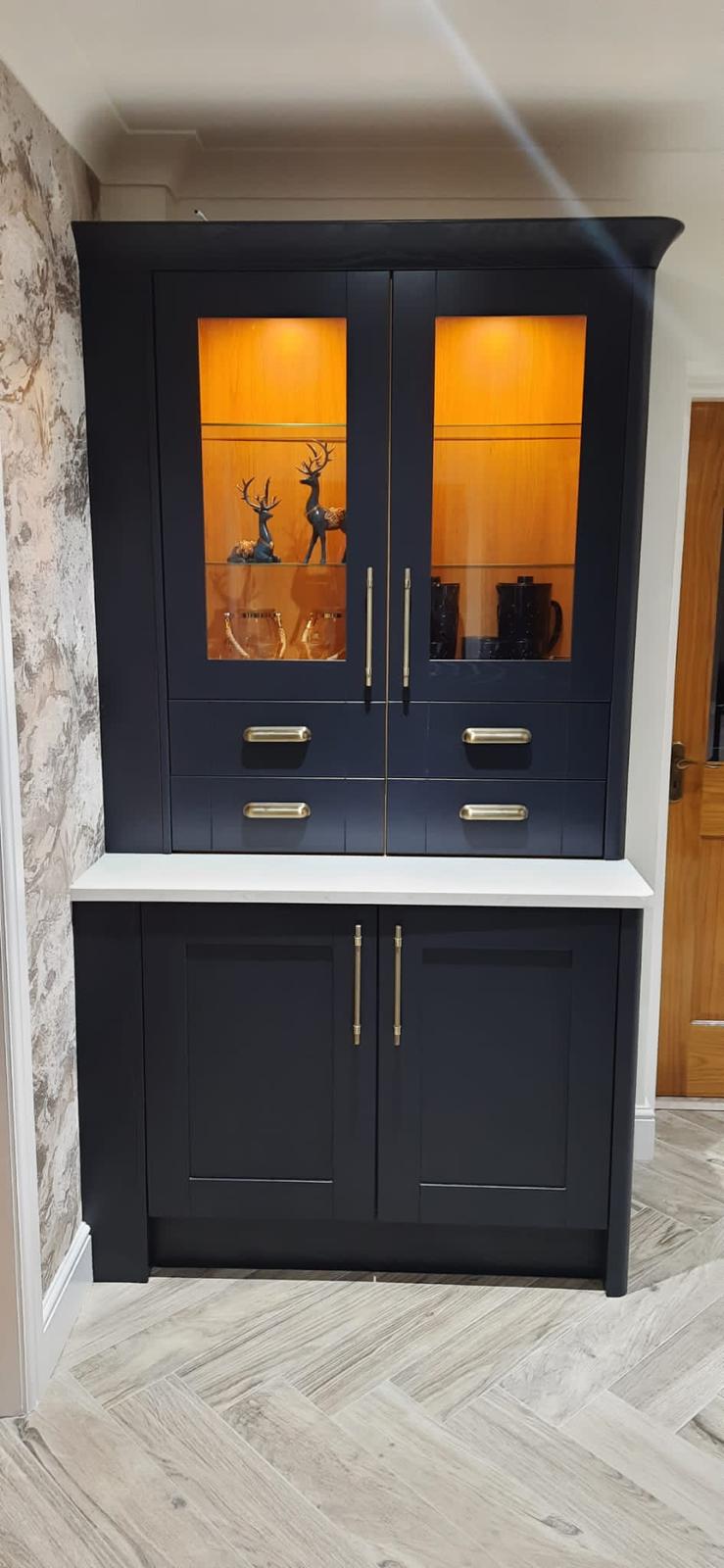 Navy dresser cabinet with brass cup handles and warm interior lighting