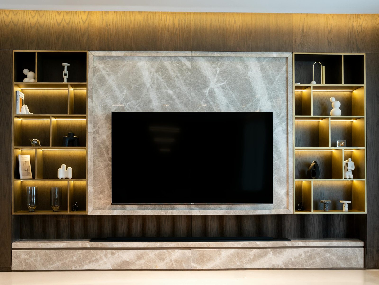 Brass-edged display niches with internal lighting flanking a wall-mounted TV